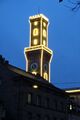 Gebäude <!--LINK'" 0:14--> dahinter beleuchteter Rathausturm bei Nacht im Dez. 2022 - die Beleuchtung des Rathauses sollte 1989 aus nicht mehr zeitgemäßen Gründen abgeschaltet werden unter der Bezeichnung "beleuchteter Mississippi Dampfer", was aber von der Bevölkerung abgelehnt wurde.