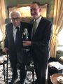 OB  übergibt <a class="mw-selflink selflink">Henry Kissinger</a> in dessen New Yorker Wohnung am   zum 95. Geburtstag eine Pappmaché Figur von 