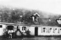 das alte, 1958 abgerissene Bauernhaus heute  mit Besitzer Friedrich Schneider, Ehefrau Maria Appolonia und oben am Fenster Tochter Kätha, Aufnahme von 1910